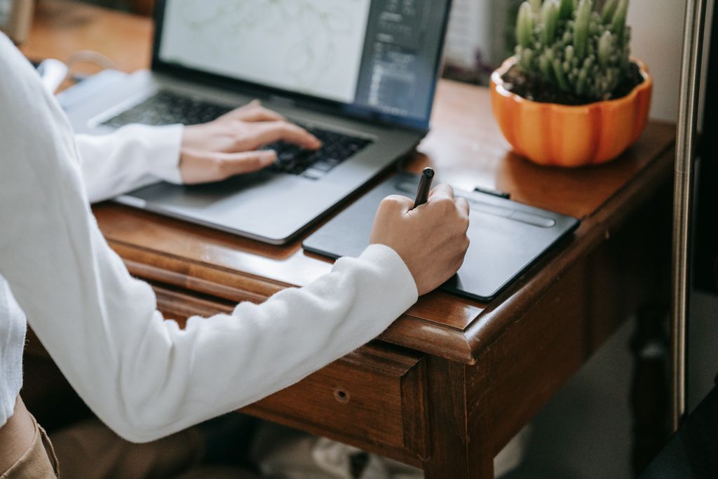 Close-up of designer working on graphics tablet with laptop, enhancing creativity and digital work.